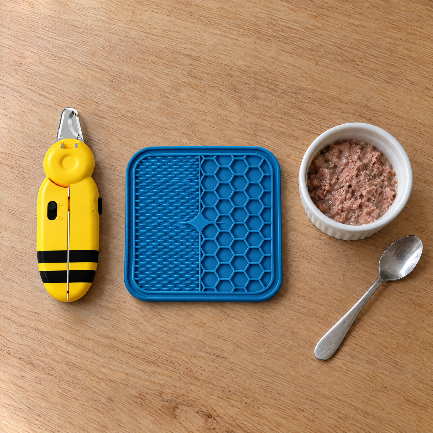 The Calm Trim Kit laid out: a yellow and black bee-striped LED cat nail clipper and a blue silicone suction lick mat